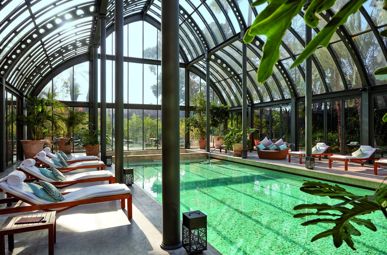 Verwarmd binnenzwembad met ligbedden onder een glazen orangerie in de spa van Royal Mansour Marrakech