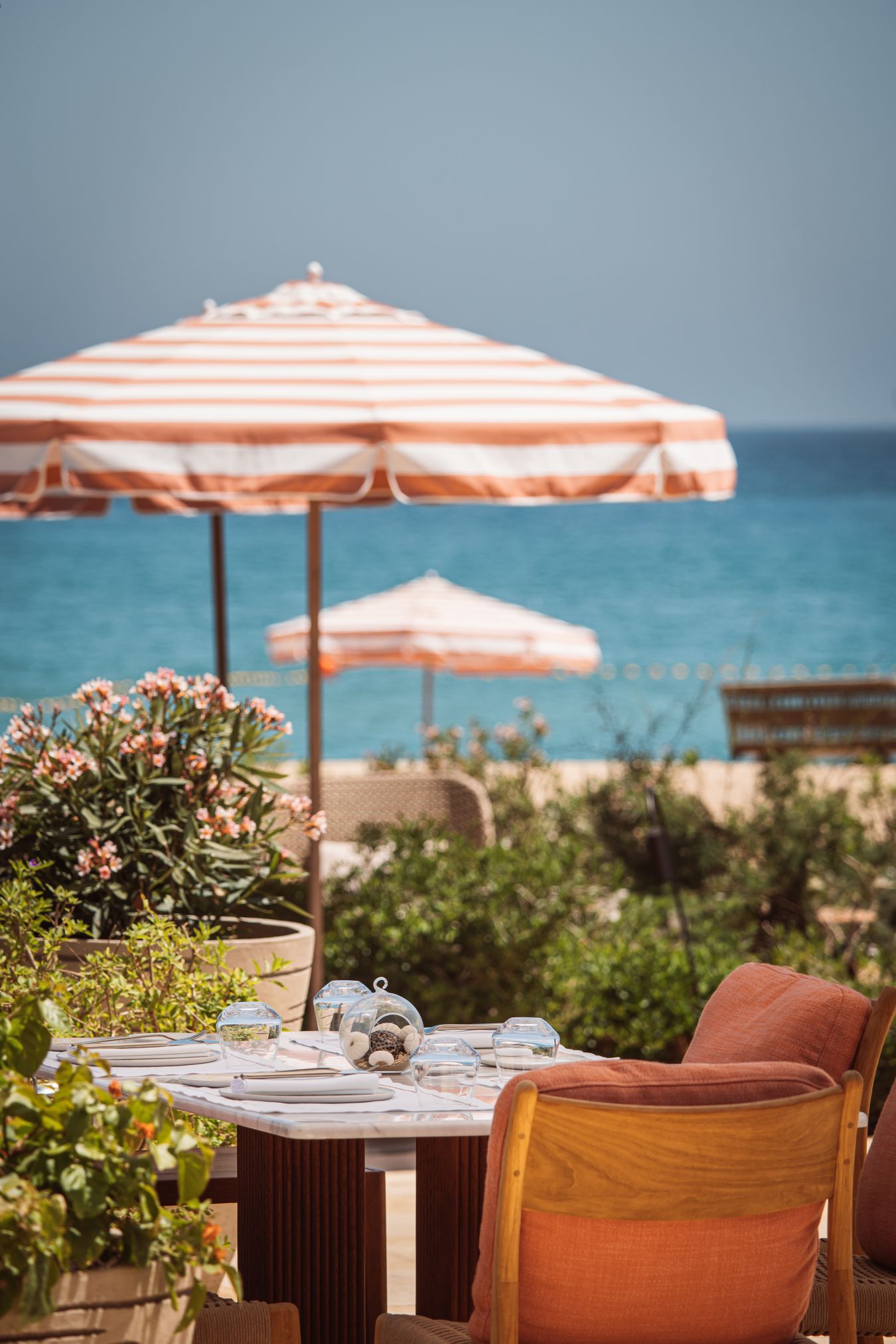 Gedekte tafel op een terras met oleanders en gestreepte parasols, met de Middellandse Zee op de achtergrond in Royal Mansour Tamuda Bay