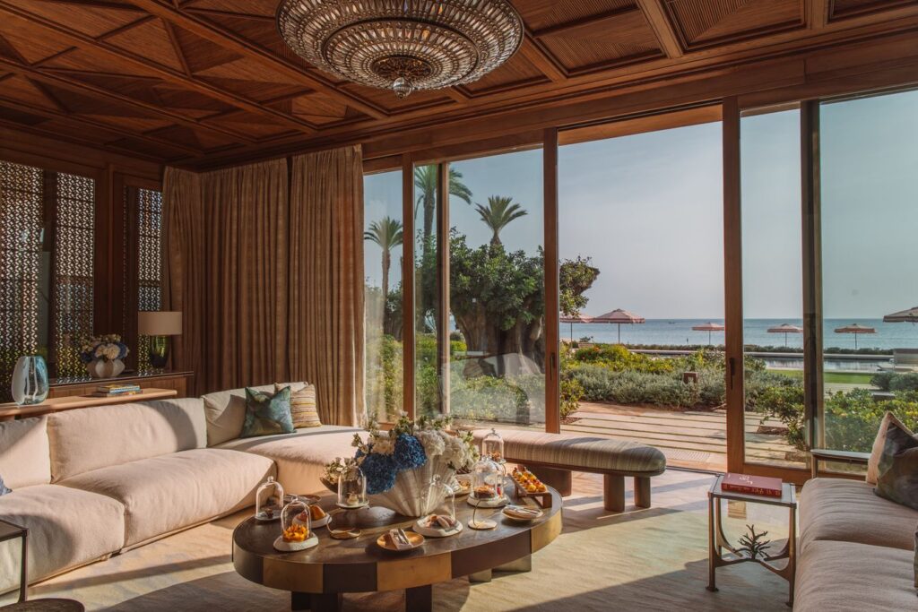 Lounge van een villa met houten plafond en grote schuiframen die uitkijken op de tuin, het strand en de Middellandse Zee in Royal Mansour Tamuda Bay
