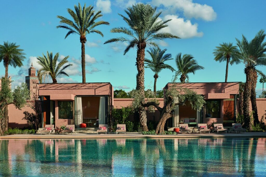 Zwembad met paviljoens in roze pisé, palmbomen en olijfbomen, met de Koutoubia-minaret op de achtergrond in Royal Mansour Marrakech